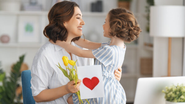 Mother holding child while browsing Mother's Day email marketing campaigns on her laptop.