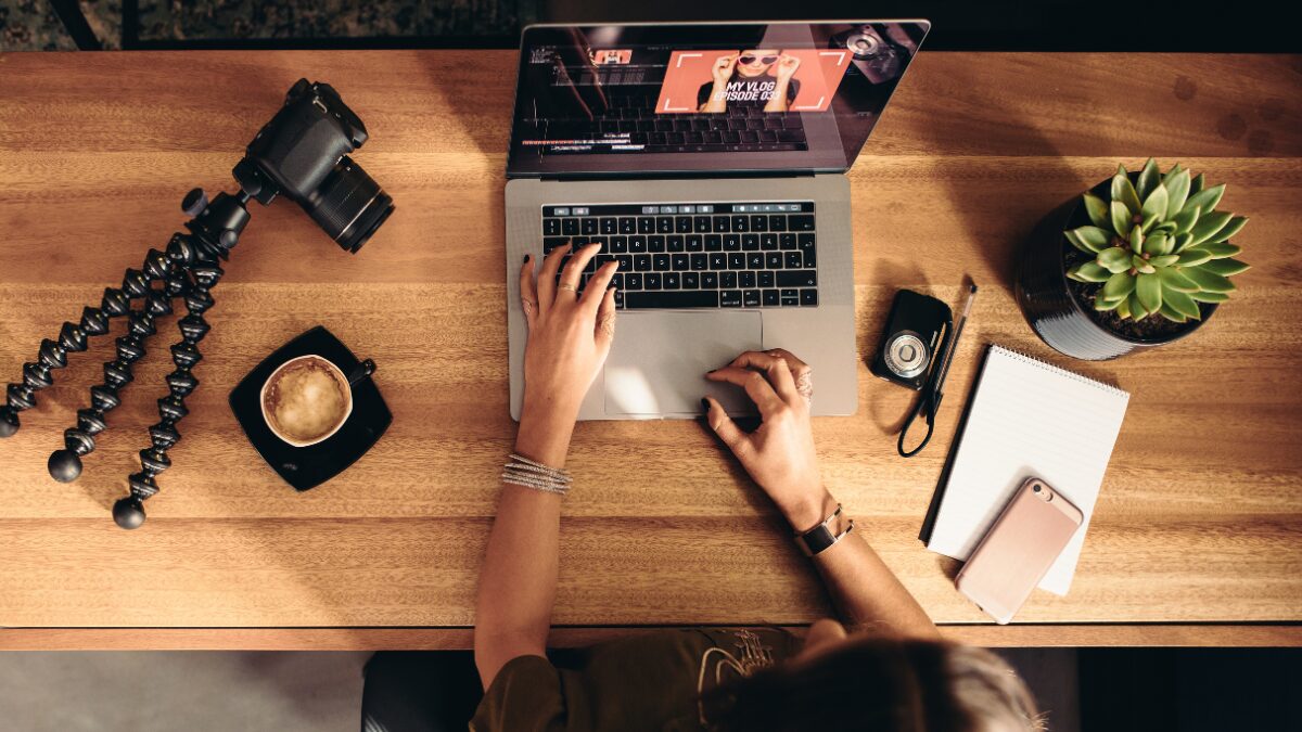 A bird’s-eye view of a person working on a laptop at a desk, surrounded by a notebook, coffee cup, and work essentials.