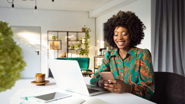 Woman working on laptop and looking at her phone smiling