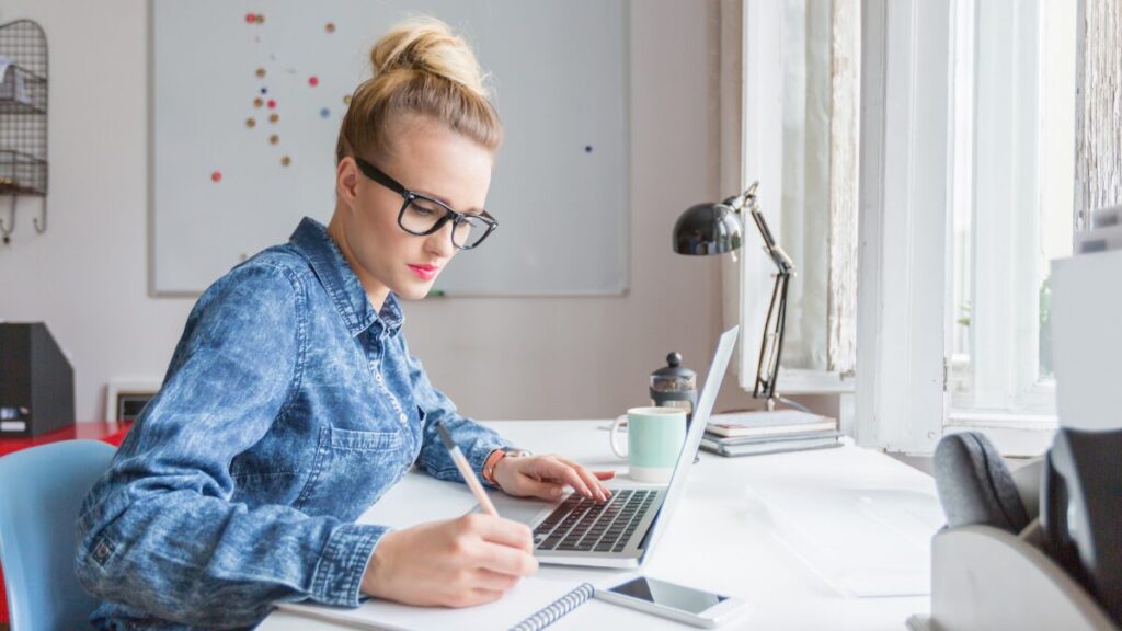 Woman working on laptop and writing notes on paper