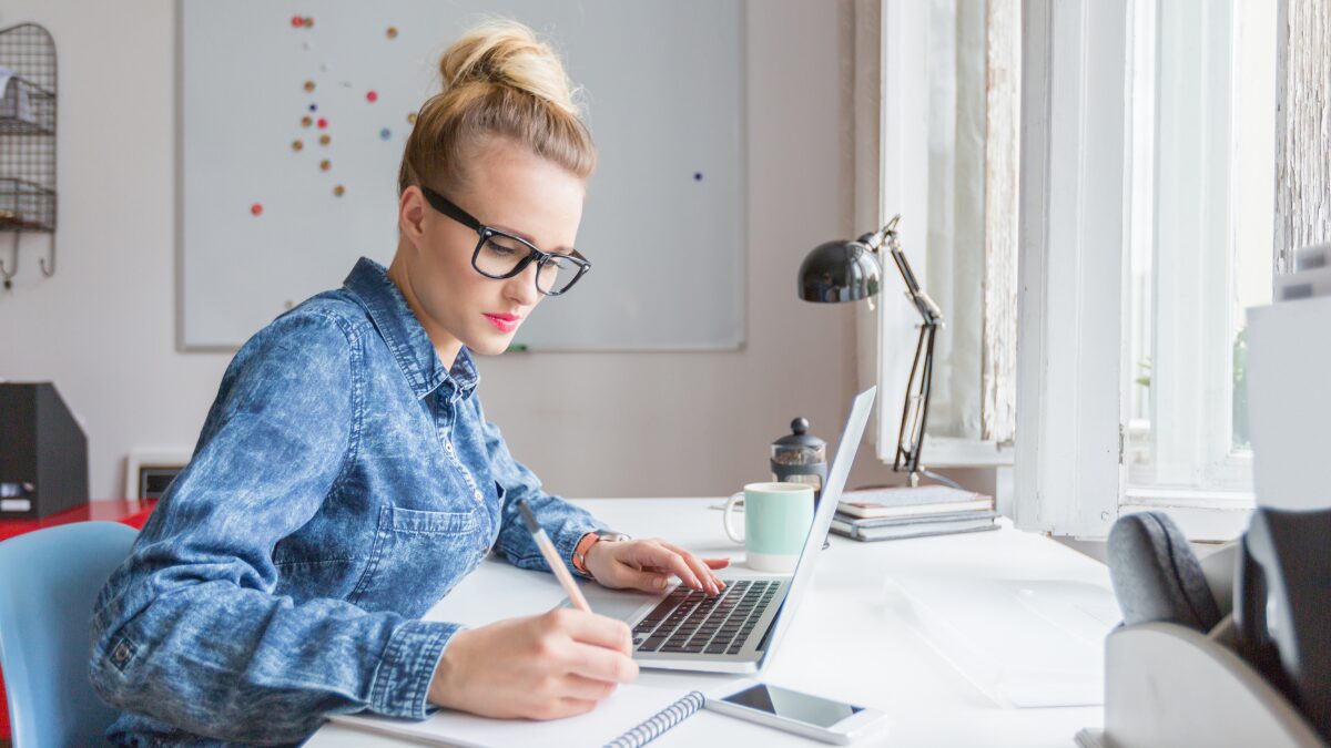 Woman working on laptop and writing notes on paper