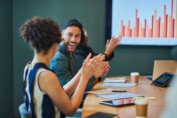 Two people in a meeting smiling and claping with data results in the background