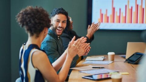 Two people in a meeting smiling and claping with data results in the background