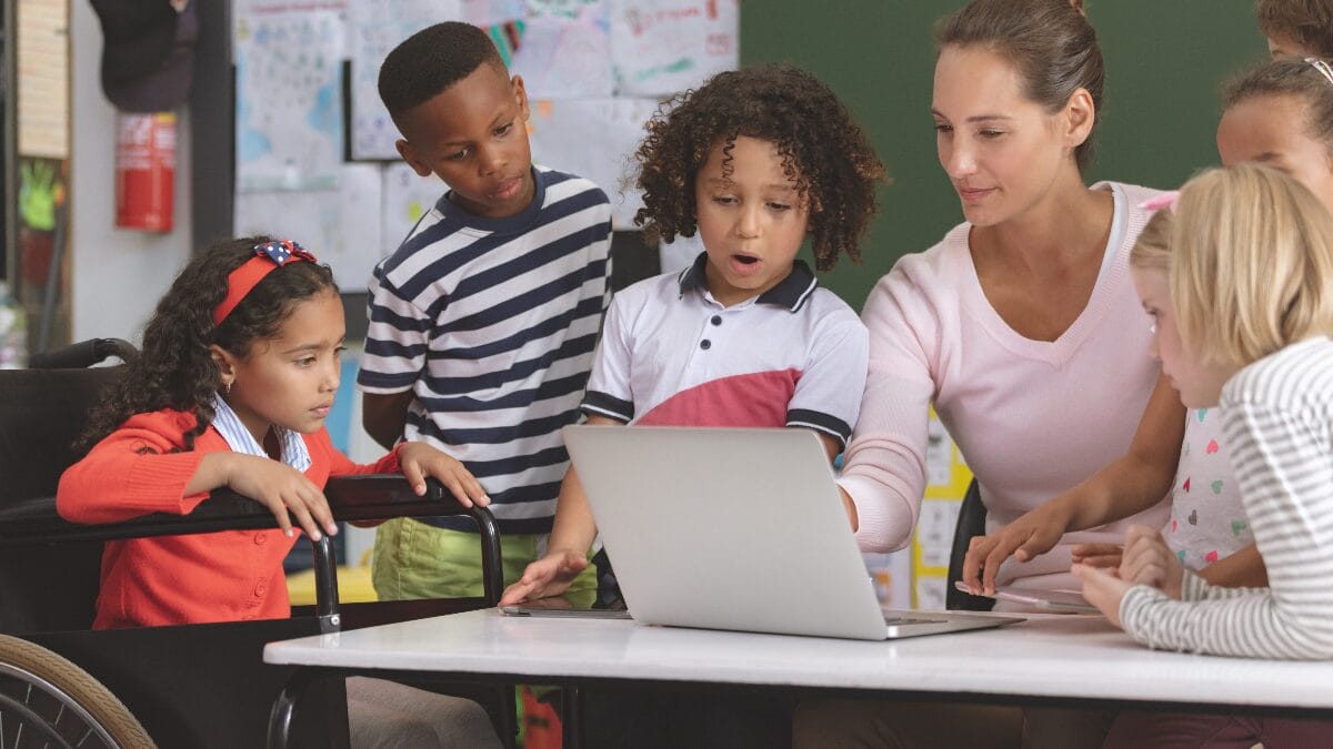 Teacher instructing children using laptop
