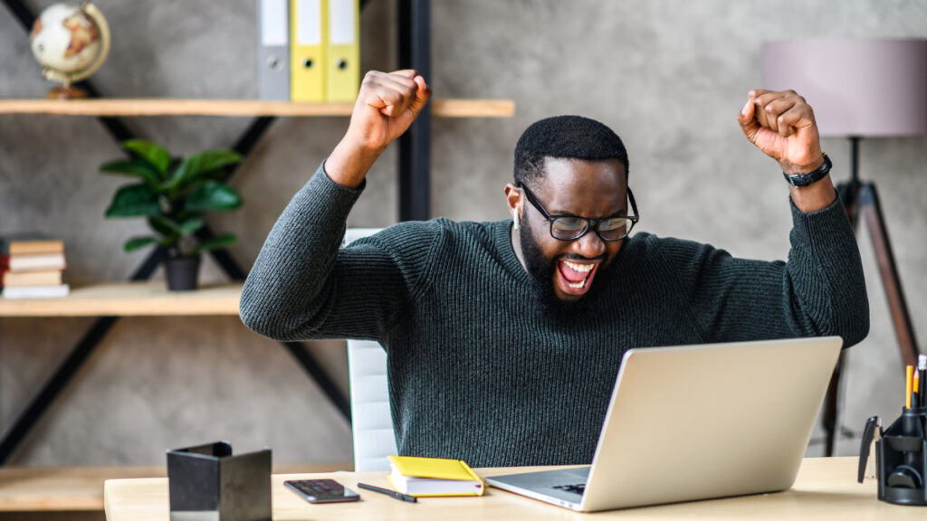 Man celebrates whilst looking at laptop